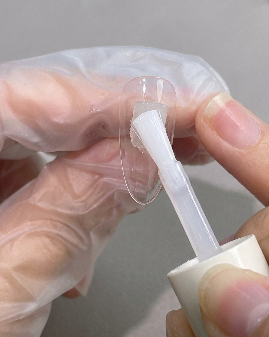 Un pincel aplicando blooming gel transparente de forma diagonal sobre la uña.