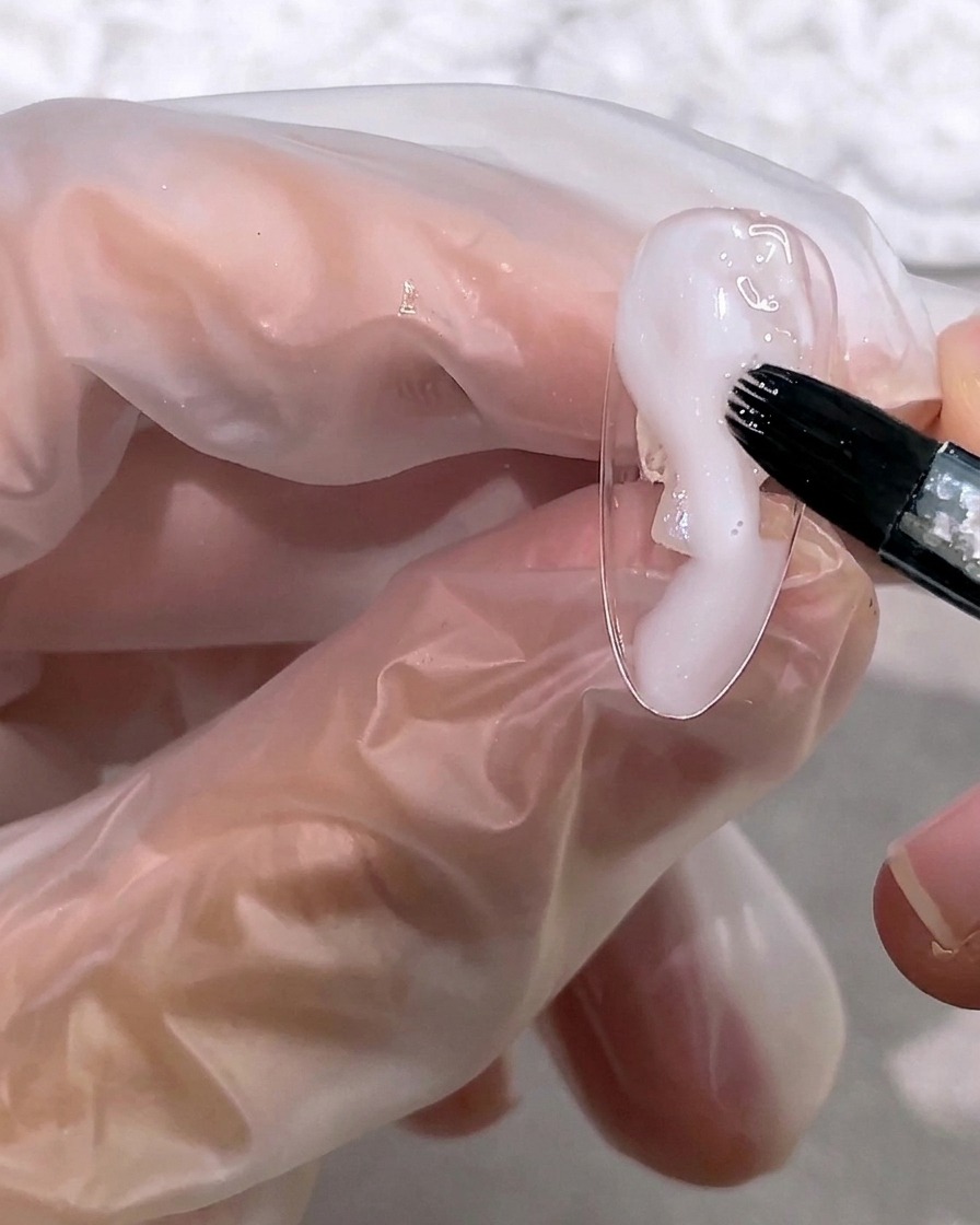 Un pincel aplicando una pequeña cantidad de gel blanco lechoso en la punta de la uña.
