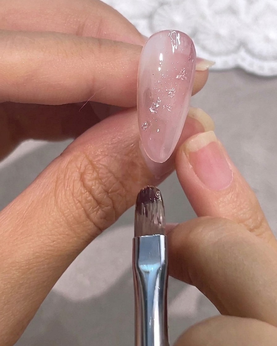 Un pincel de detalle sobre una uña rosa brillante con acentos plateados.