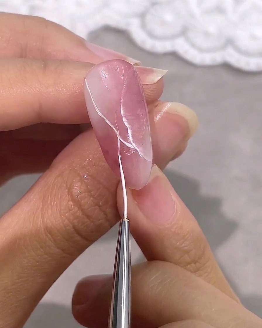 Un pincel liner añadiendo vetas blancas delicadas a un diseño marmolado.
