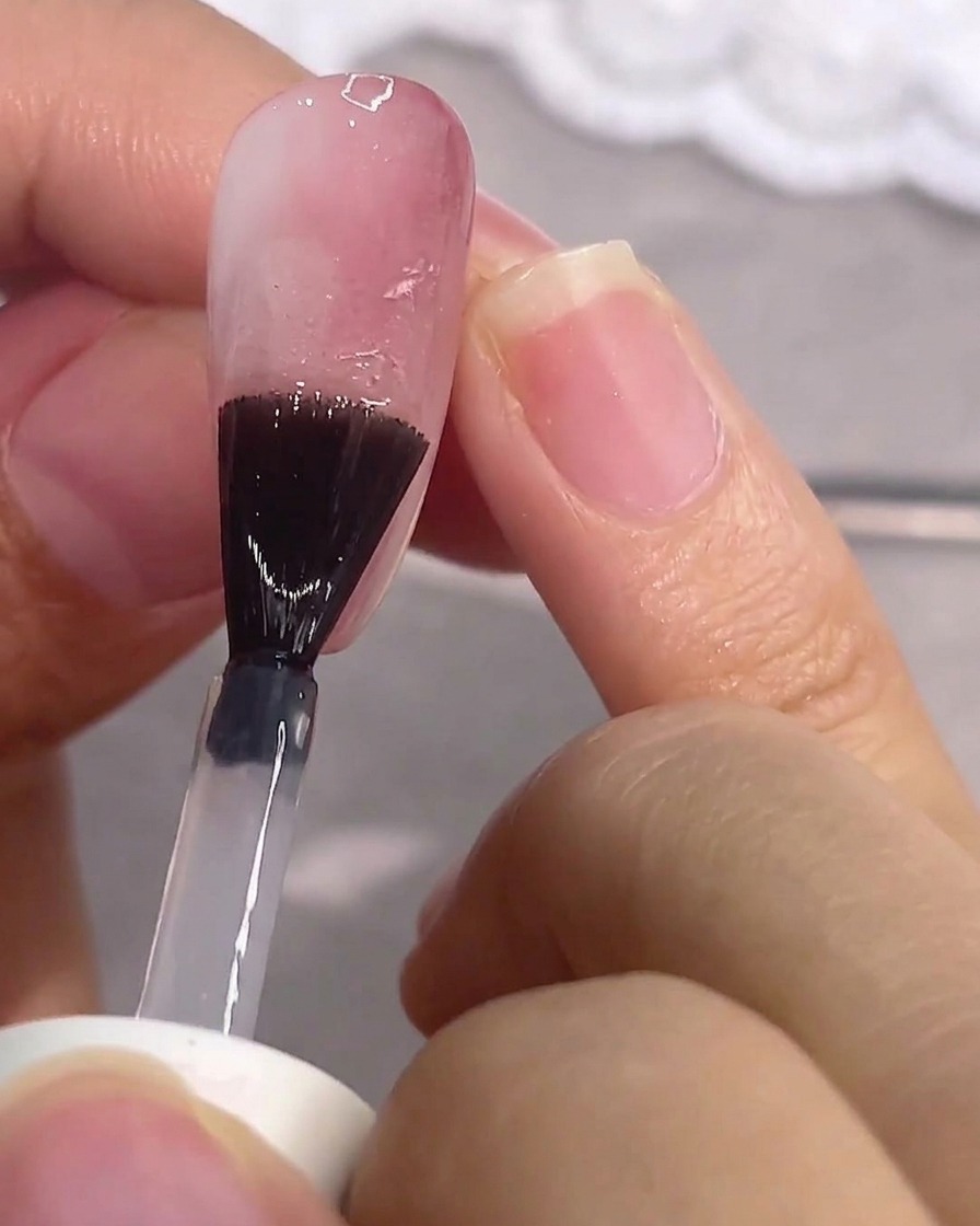 Un pincel aplicando top coat mate sobre una uña rosa.