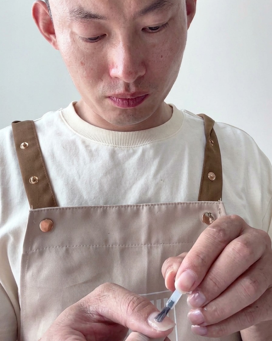 Pincel aplicando esmalte en gel blanco lechoso traslúcido sobre una uña preparada.