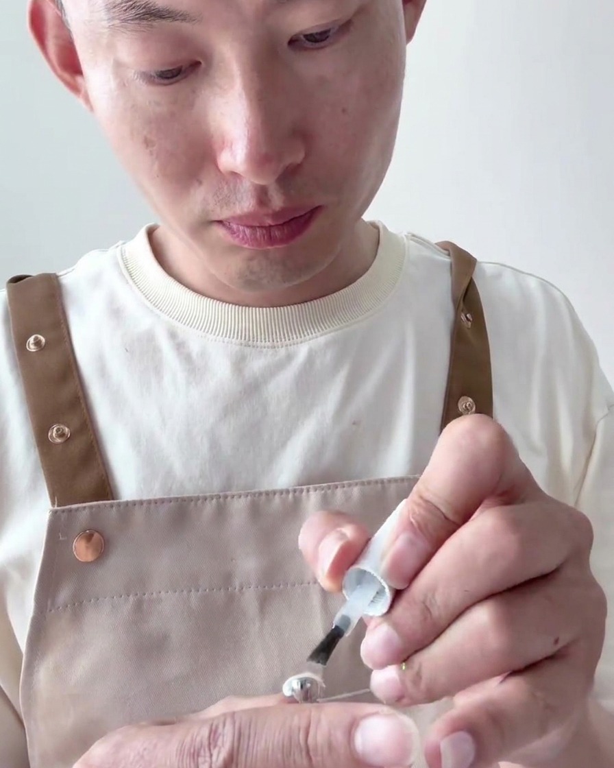 Primer plano de un pincel aplicando una segunda capa de esmalte en gel blanco lechoso opaco sobre la uña.