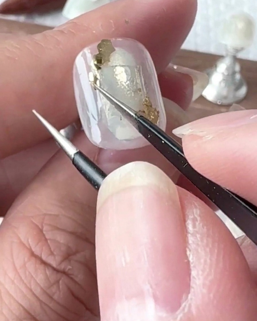 Un pincel de detalle pequeño aplicando diminutas gotas de gel transparente sobre la superficie de una uña pintada.