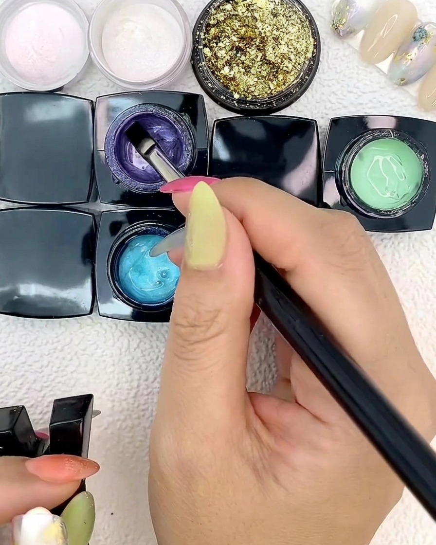 Un pincel plano de arte de uñas aplicando gel azul sobre una punta de uña.