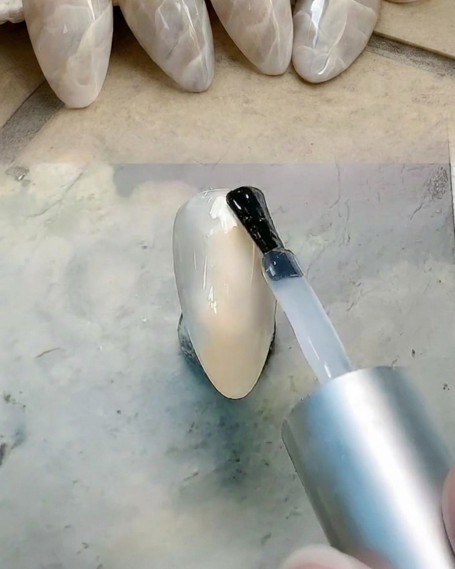 Un pincel aplicando una capa de gel transparente sobre la superficie de la uña para prepararla para el difuminado.