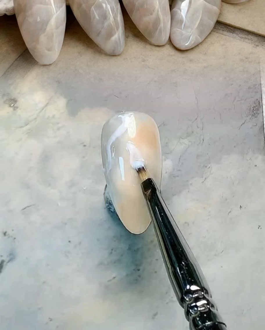 Un pincel plano mezclando los colores de gel marrón y gris en la uña para crear un degradado suave.