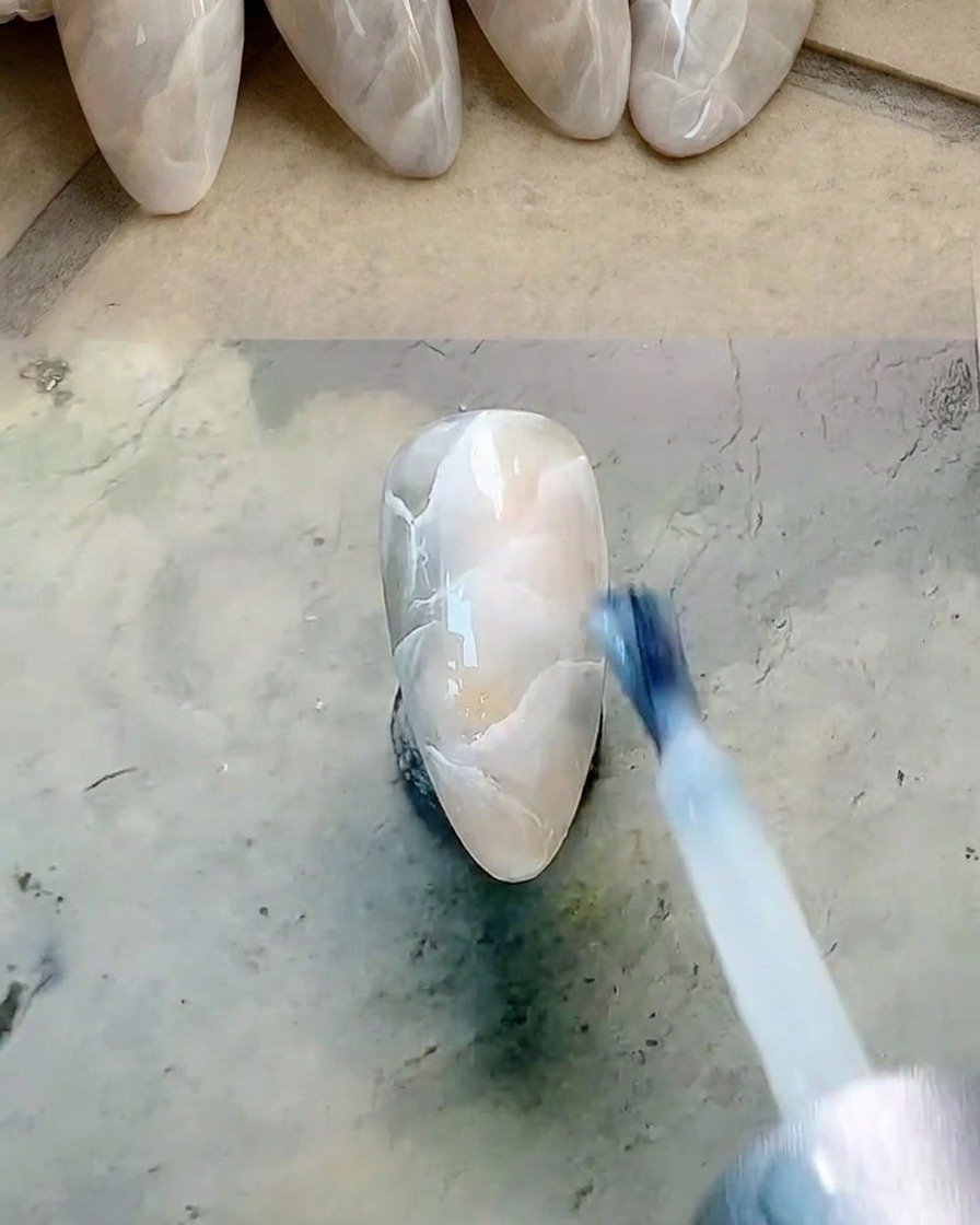 Un pincel plano aplicando una fina capa de esmalte en gel blanco lechoso translúcido sobre una uña marmoleada.