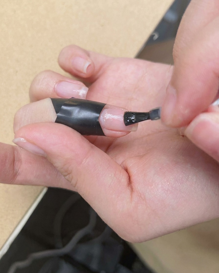 Un pincel de detalle fino aplicando un punto de esmalte rosa vibrante en el centro de una uña cubierta con blooming gel húmedo.