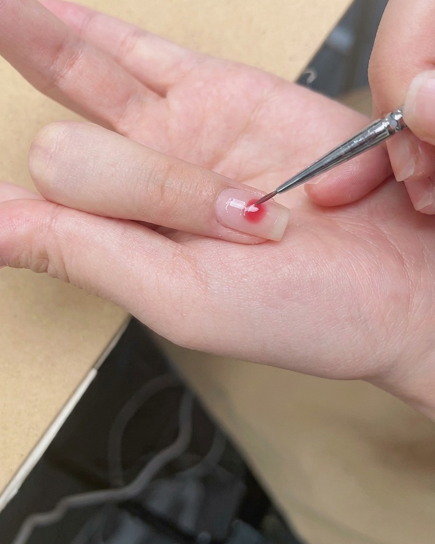 Un pincel de detalle fino difuminando los bordes de un punto rosa central para crear un suave ombré efecto rubor.