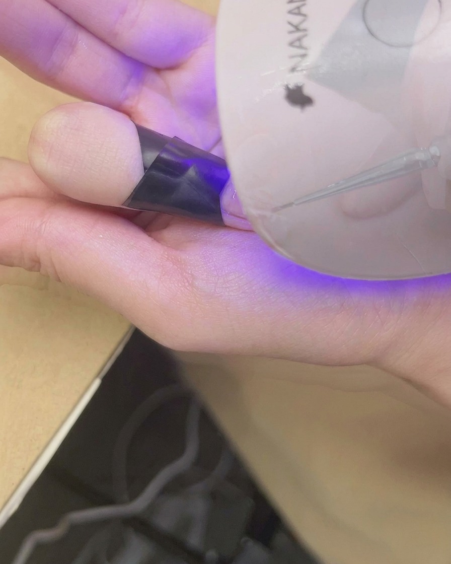 Un dedo colocado bajo una mini lámpara UV/LED para curar el nail art con degradado blush terminado.