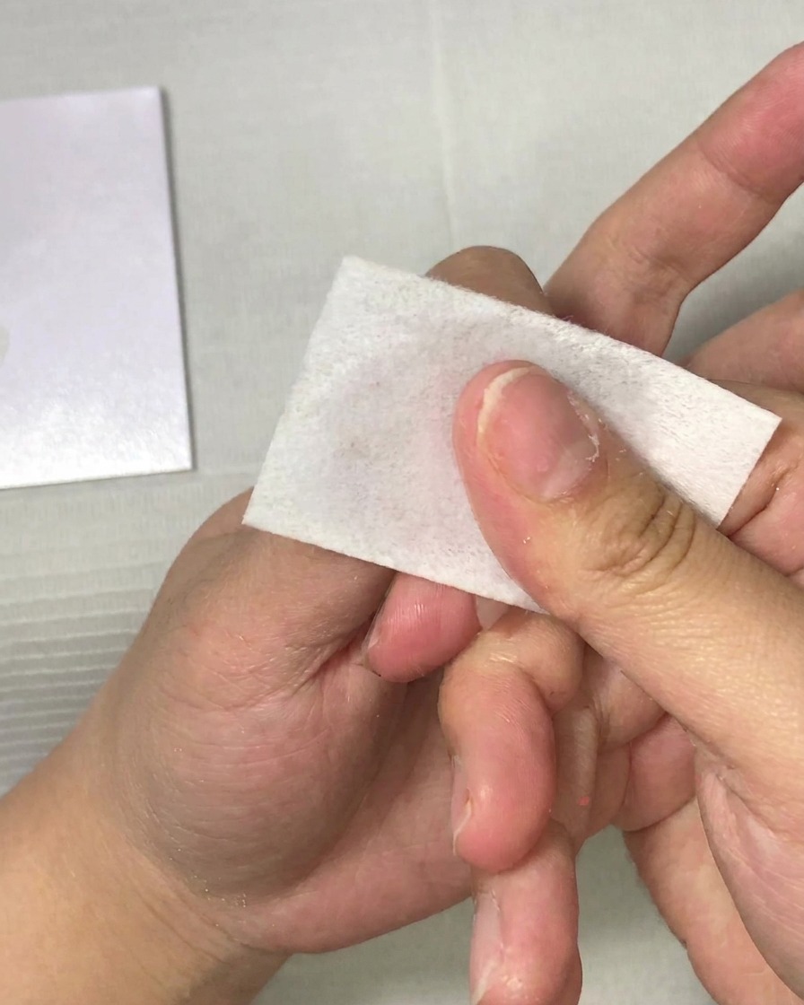Primer plano de una mano utilizando una toallita sin pelusa para limpiar una uña.