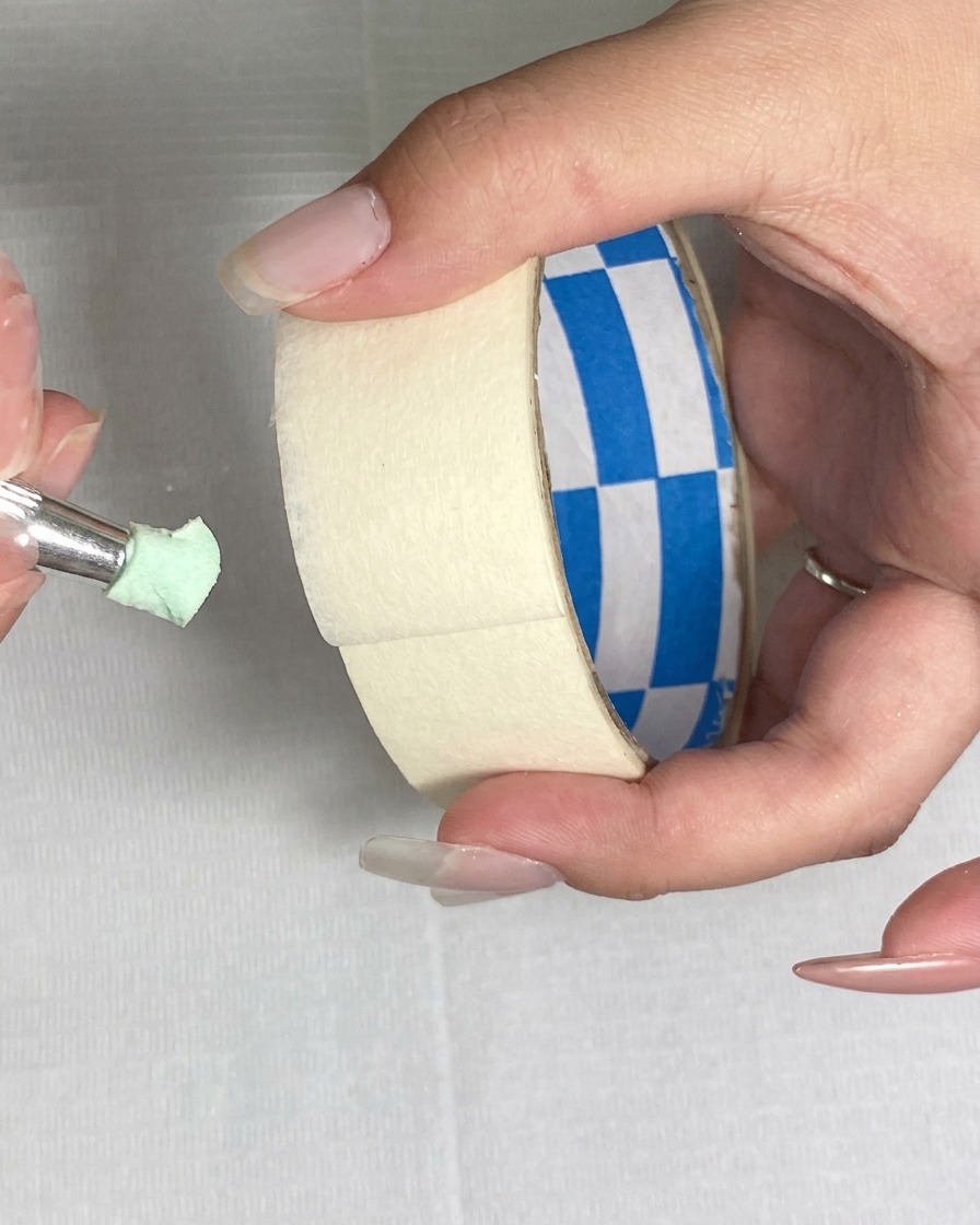 Uso de una pieza de cinta adhesiva para levantar partículas finas de la superficie de una esponja verde.