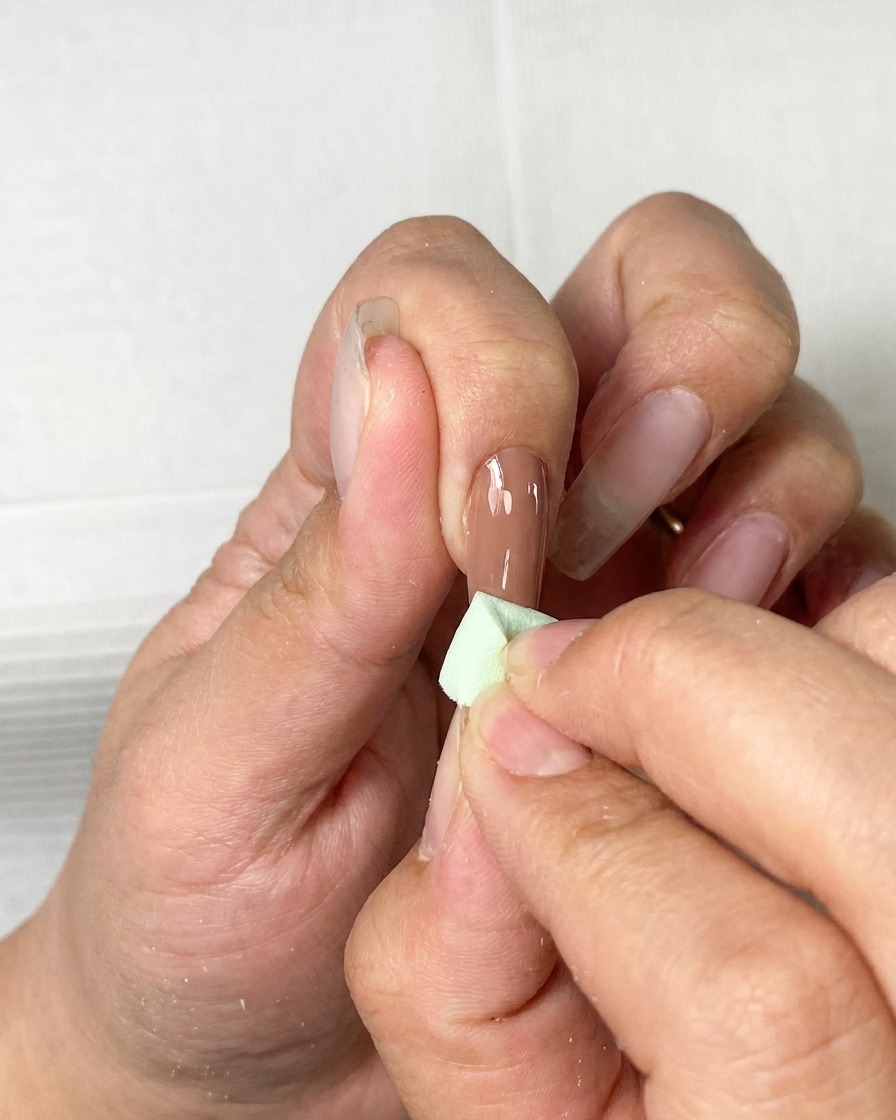Un pincel aplicando una capa suave de esmalte de gel marrón sobre una uña natural.