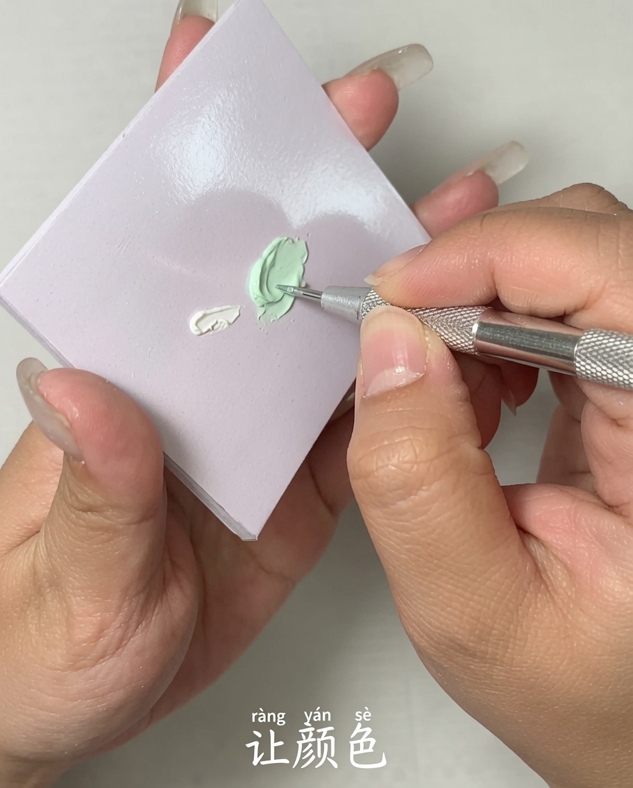 Primer plano de una herramienta de metal mezclando dos colores diferentes de esmalte de gel sobre una superficie plana de paleta.