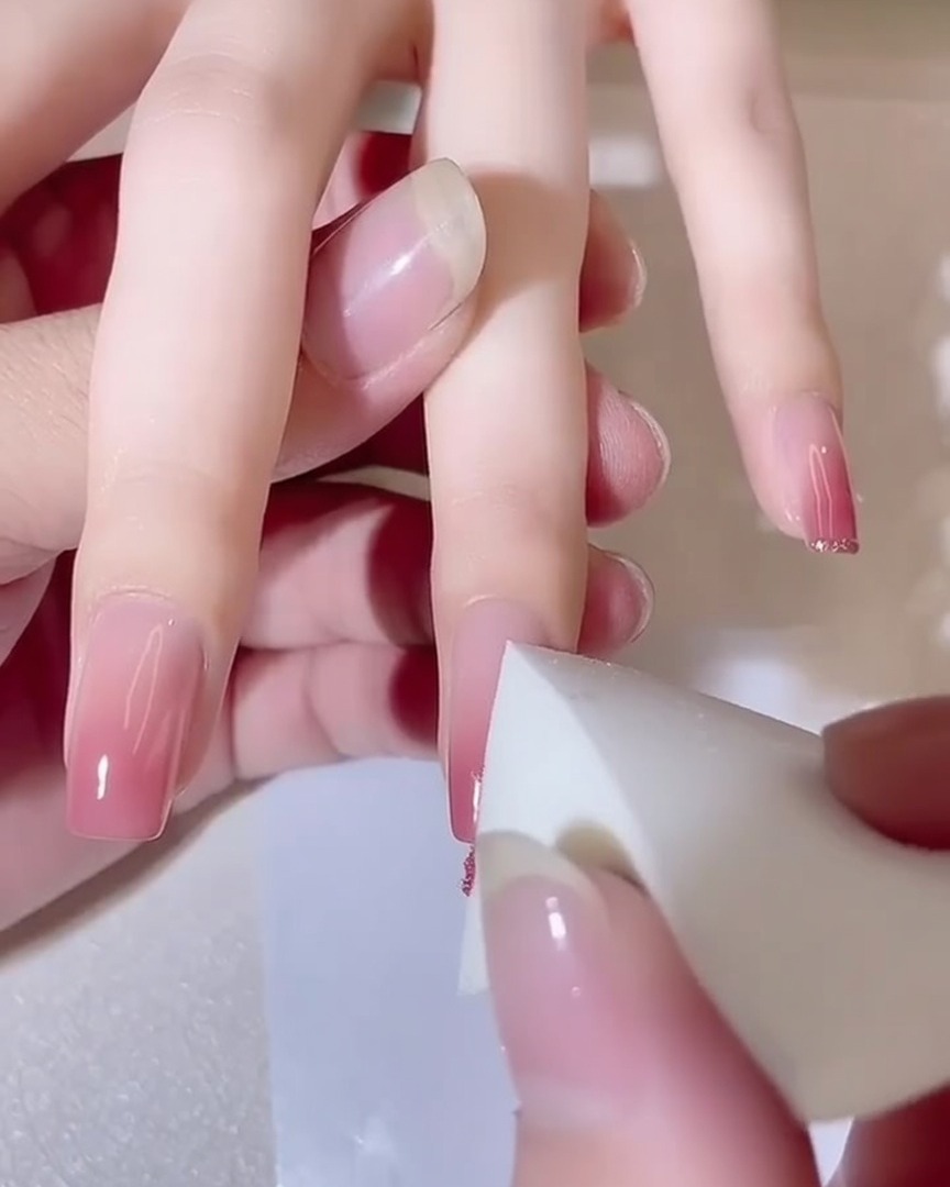 Primer plano de una esponja aplicando toques sobre una uña, mostrando un efecto de degradado rosa más profundo.