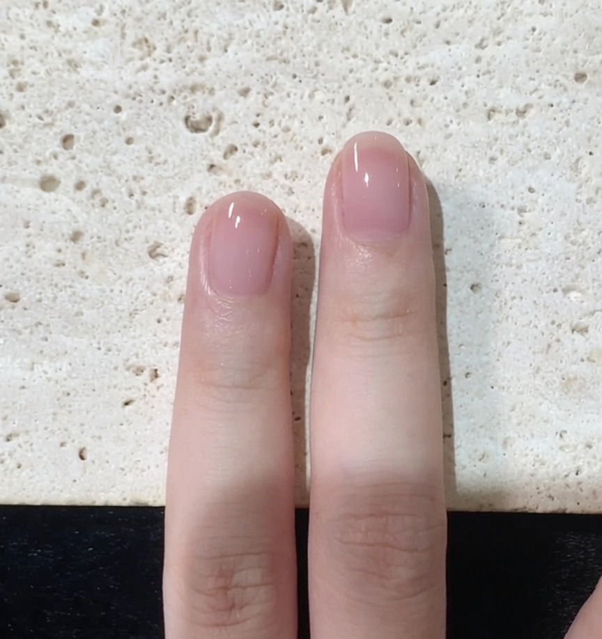Un pincel de uñas refinando cuidadosamente los bordes y la punta de una uña pintada de rosa.