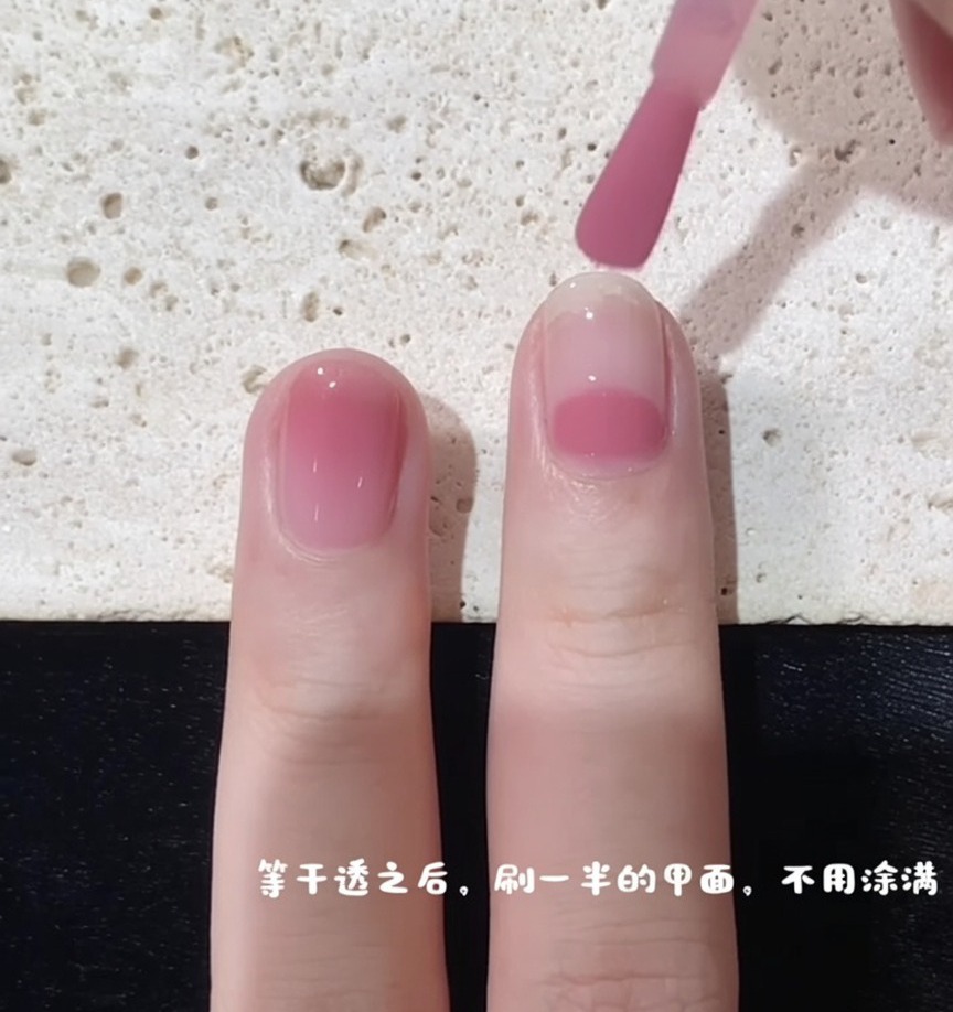 Un pincel de uñas comenzando la aplicación de esmalte rosa desde la mitad de la uña para crear el efecto degradado.