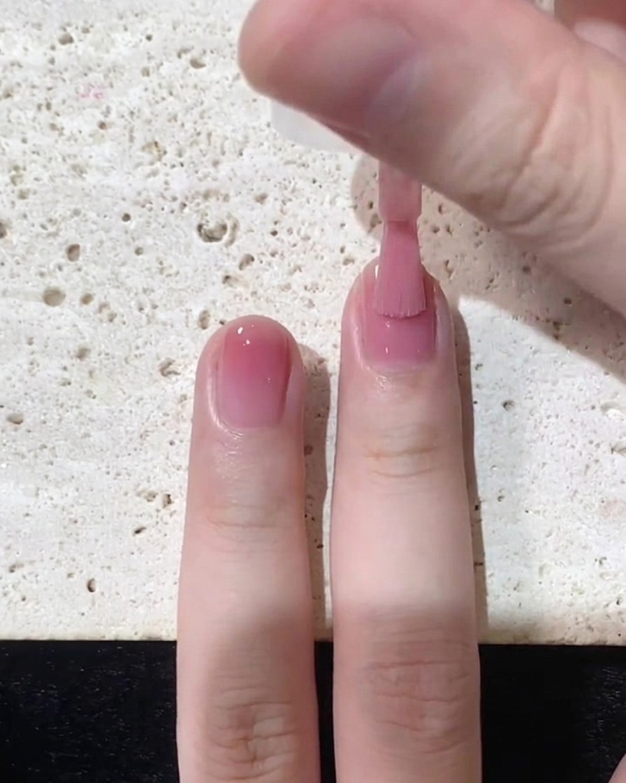 Un pincel deslizando el esmalte jelly rosa suavemente hacia el borde libre sobre la mitad superior de la uña.