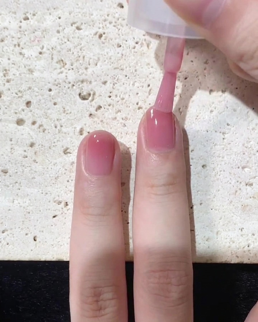 Un pincel aplicando una capa final concentrada de esmalte rosa específicamente en la punta de la uña.