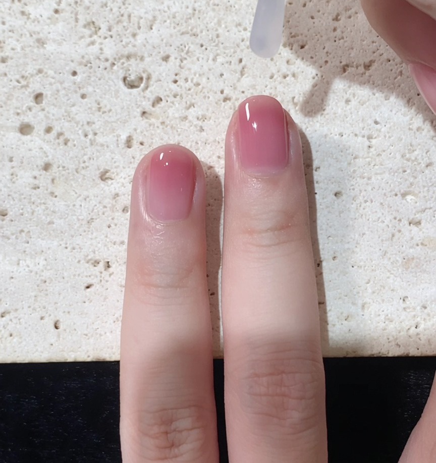 Un pincel aplicando un top coat transparente y brillante sobre el diseño de uña degradada terminado.