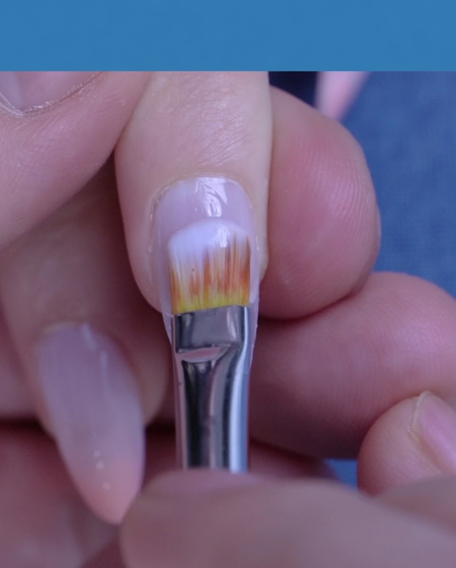 Un pincel aplicando esmalte de gel blanco lechoso y traslúcido sobre una uña natural.