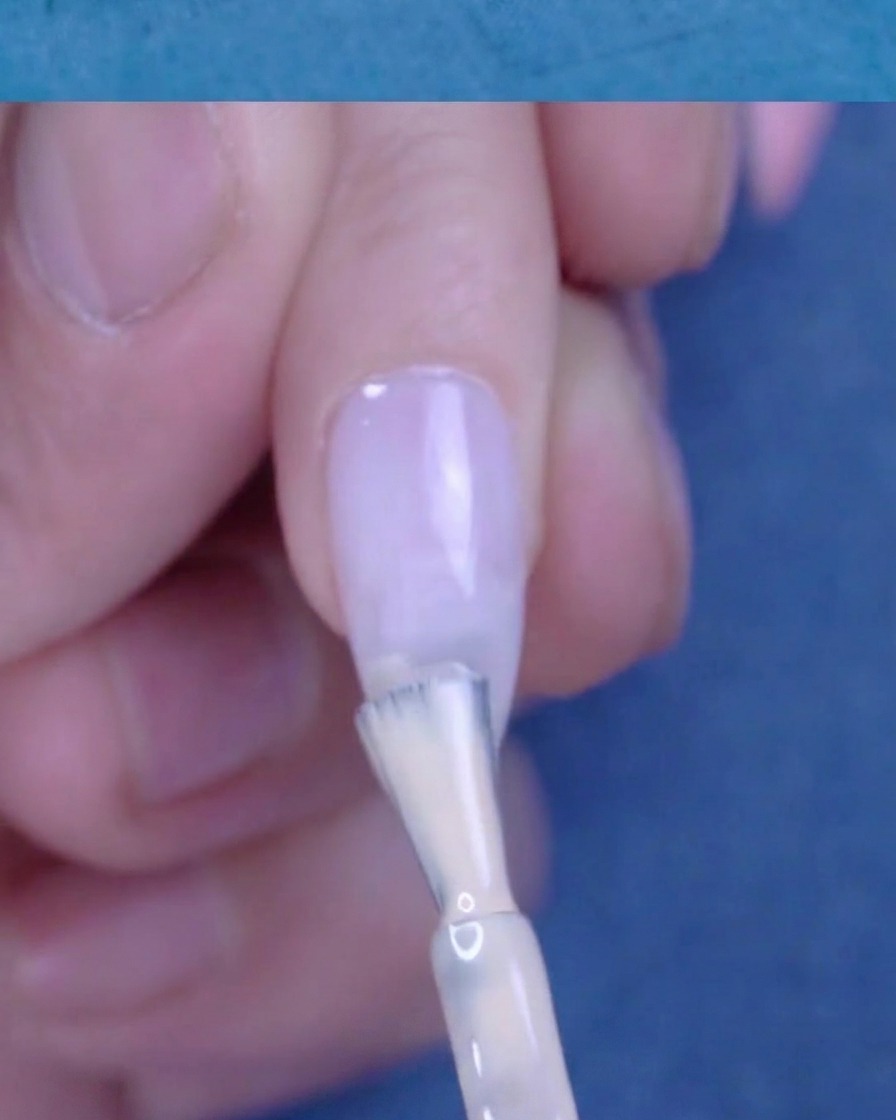 Aplicando una segunda capa más concentrada de esmalte de gel nude en la punta de la uña.