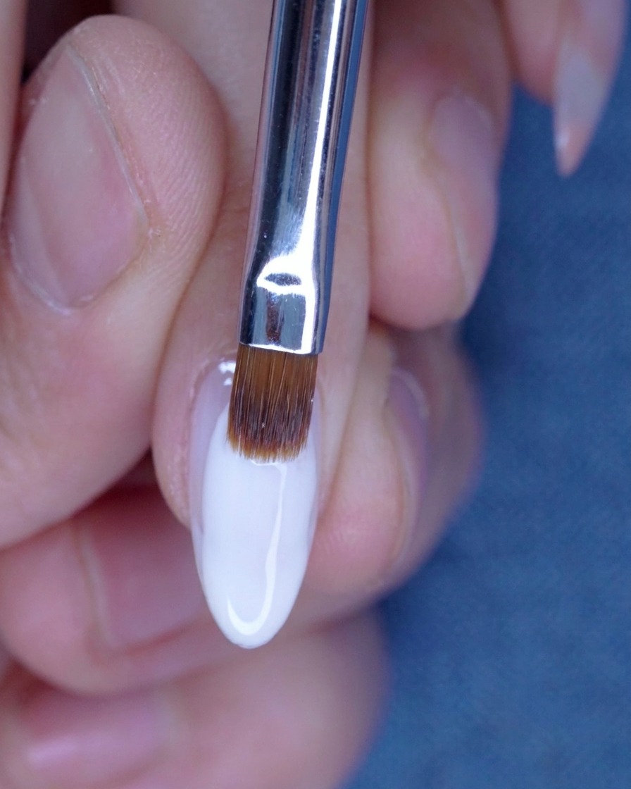 Difuminando la segunda capa de gel nude con un pincel para una transición perfecta.