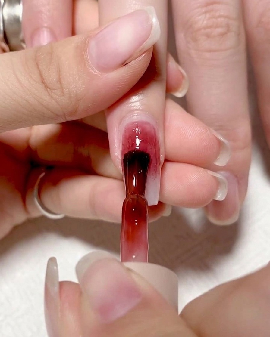 Un pincel aplicando un gel rojo vibrante en la mitad izquierda de una uña, creando un bloque de color definido.