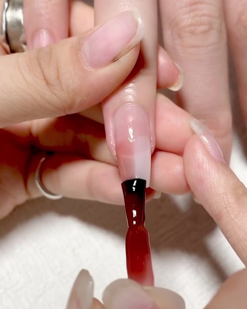 Un pincel de degradado dando toques suaves en el centro de la uña donde se encuentran el gel rojo y el transparente para suavizar la línea.