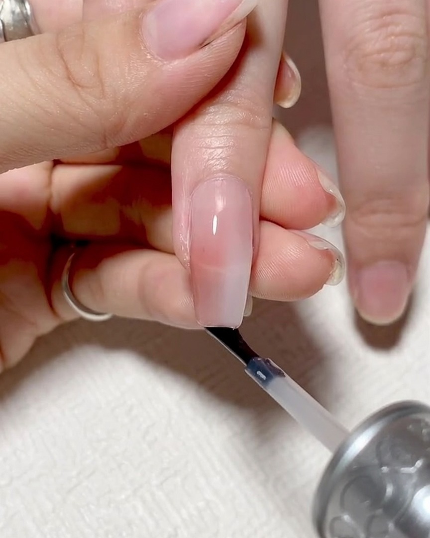 Primer plano que muestra el pincel de uñas pasando horizontalmente a lo largo del borde libre de la uña para sellarlo.