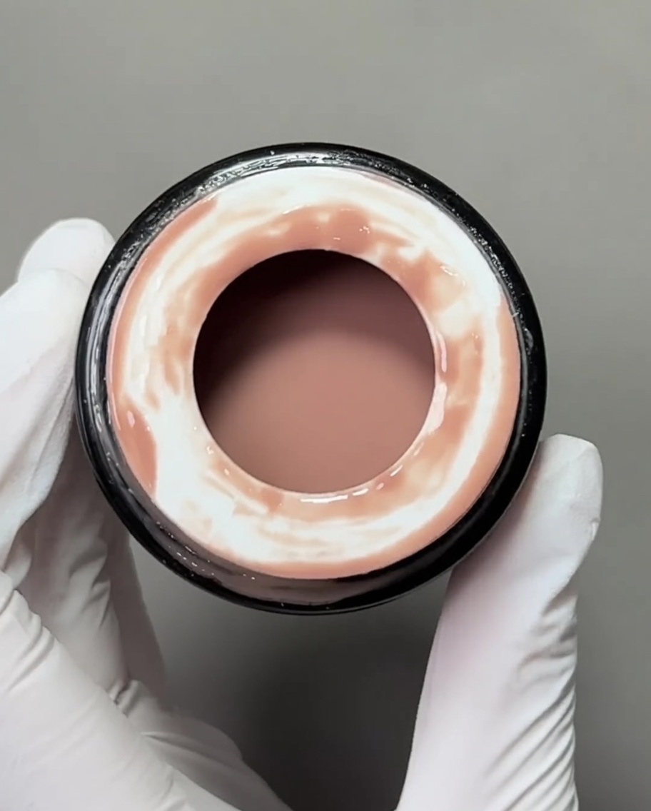 Un primer plano de un pincel plano para gel aplicando una base de gel color nude sobre un tip de uña.