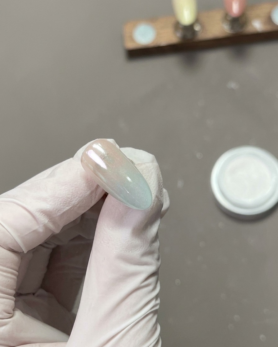 Primer plano de un dedo puliendo la superficie de una uña cubierta con polvo cromado, creando un reflejo de alto brillo.