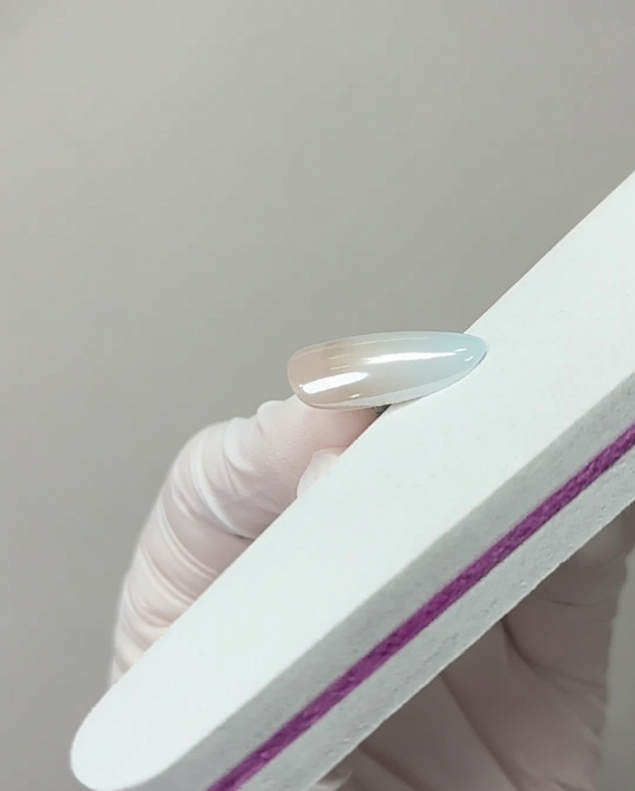 Una lima de uñas tocando ligeramente el borde libre de una uña con acabado cromado para eliminar el exceso de pigmento.