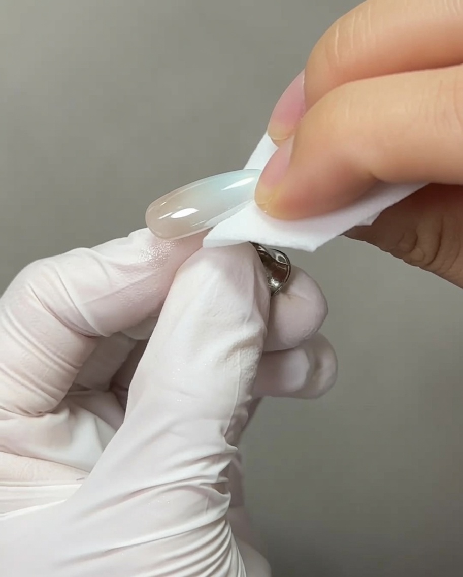 Primer plano de un pincel aplicando una perla transparente de gel de extensión en la misma punta de una uña con acabado cromado.