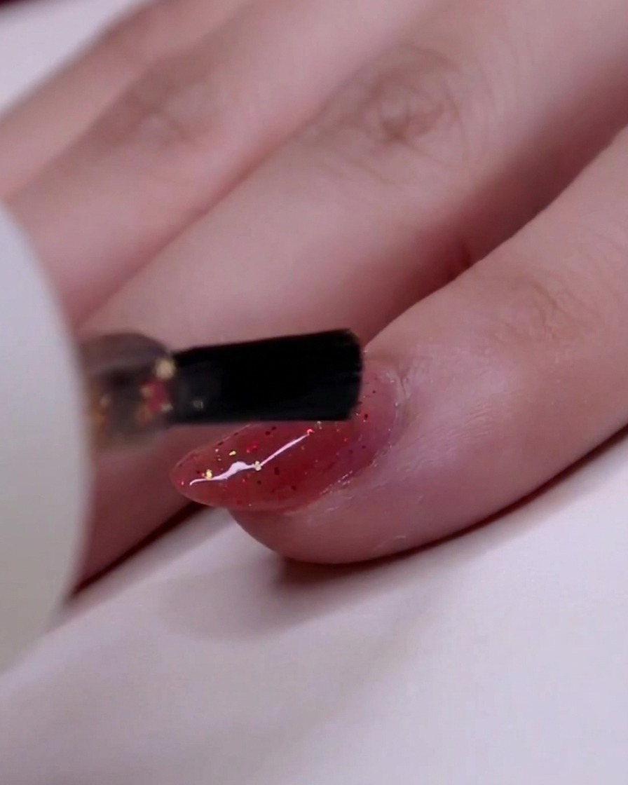 Un primer plano de un pincel aplicando esmalte de purpurina en el dedo anular, enfocándose en colocar copos dorados de forma segura.