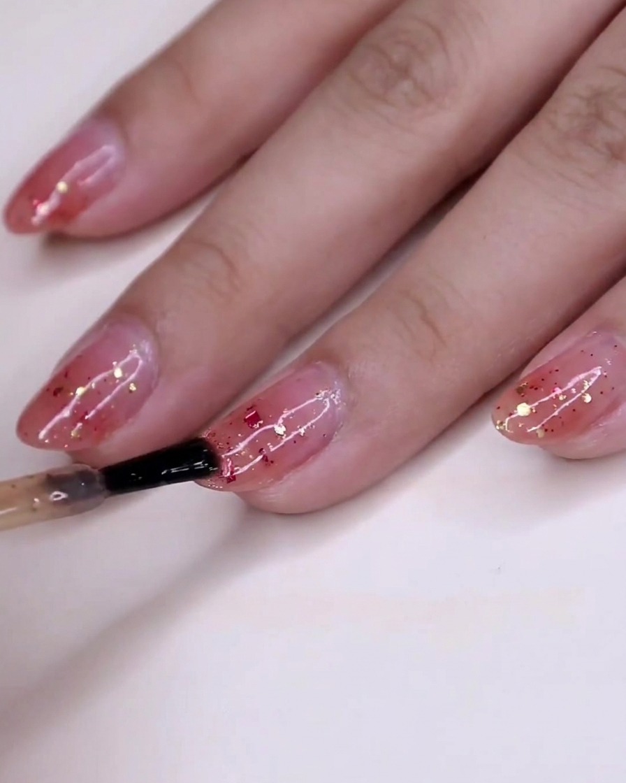 Una vista de la mano con esmalte de purpurina húmedo asentándose en las uñas sobre la base de degradado rosa.