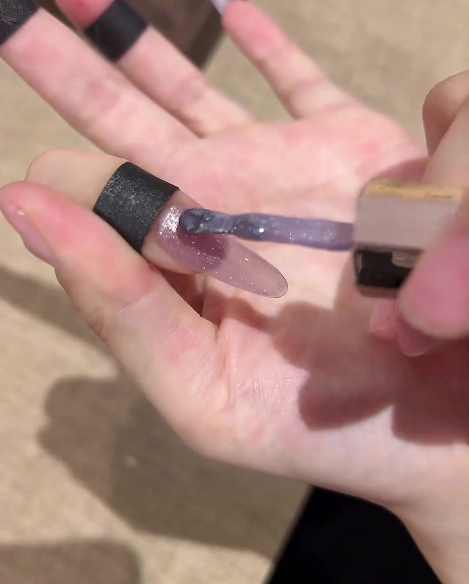 Un pincel de uñas aplicando un top coat brillante final sobre el arte de uñas galáctico completado.