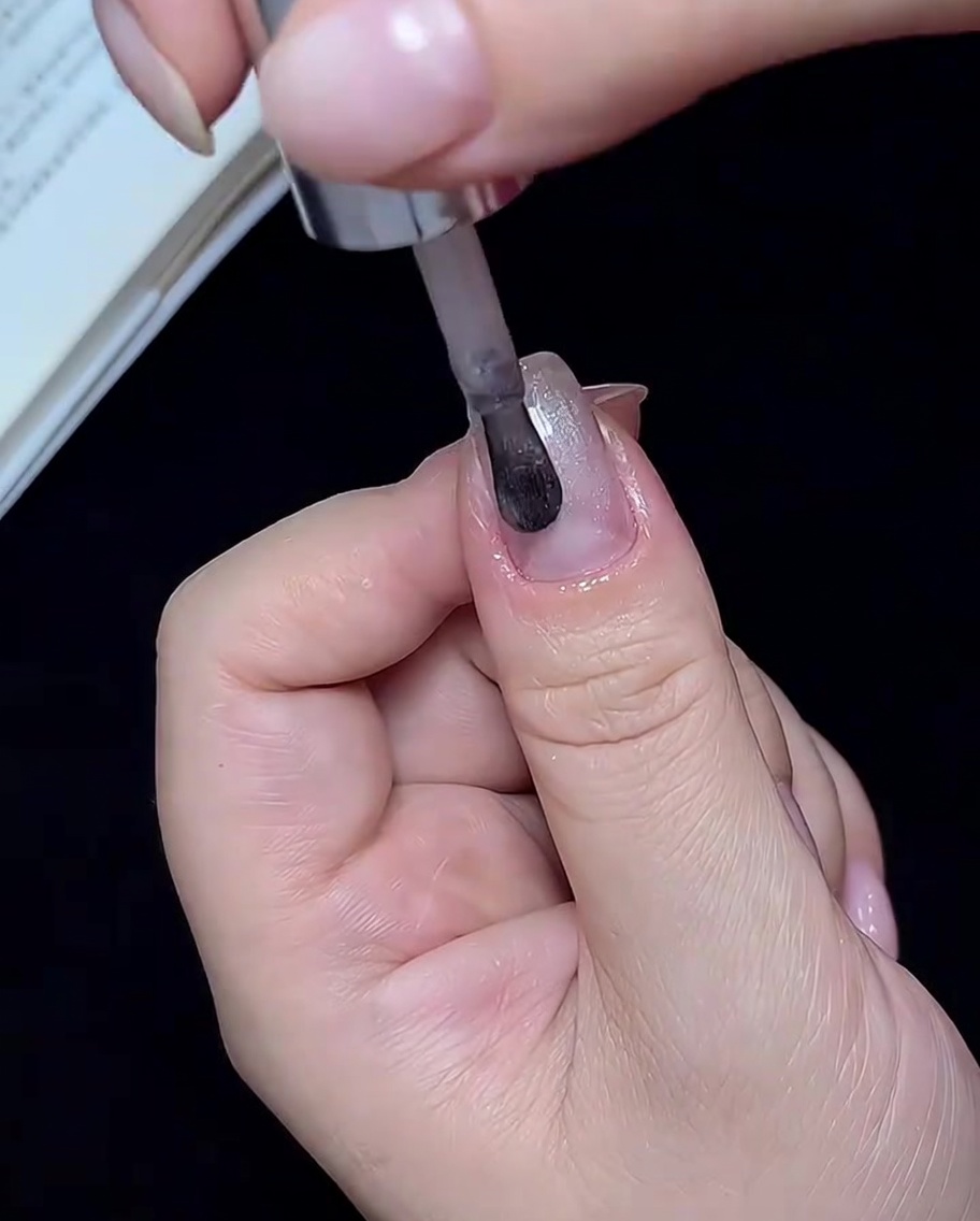 Un pincel aplicando esmalte de uñas cat-eye blanco translúcido en una sola uña.