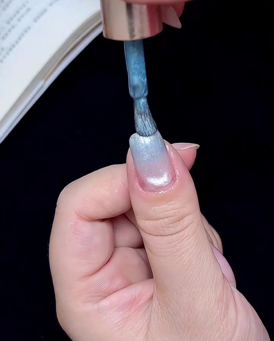 Un pincel aplicando una pequeña cantidad de gel azul en la punta de la uña.