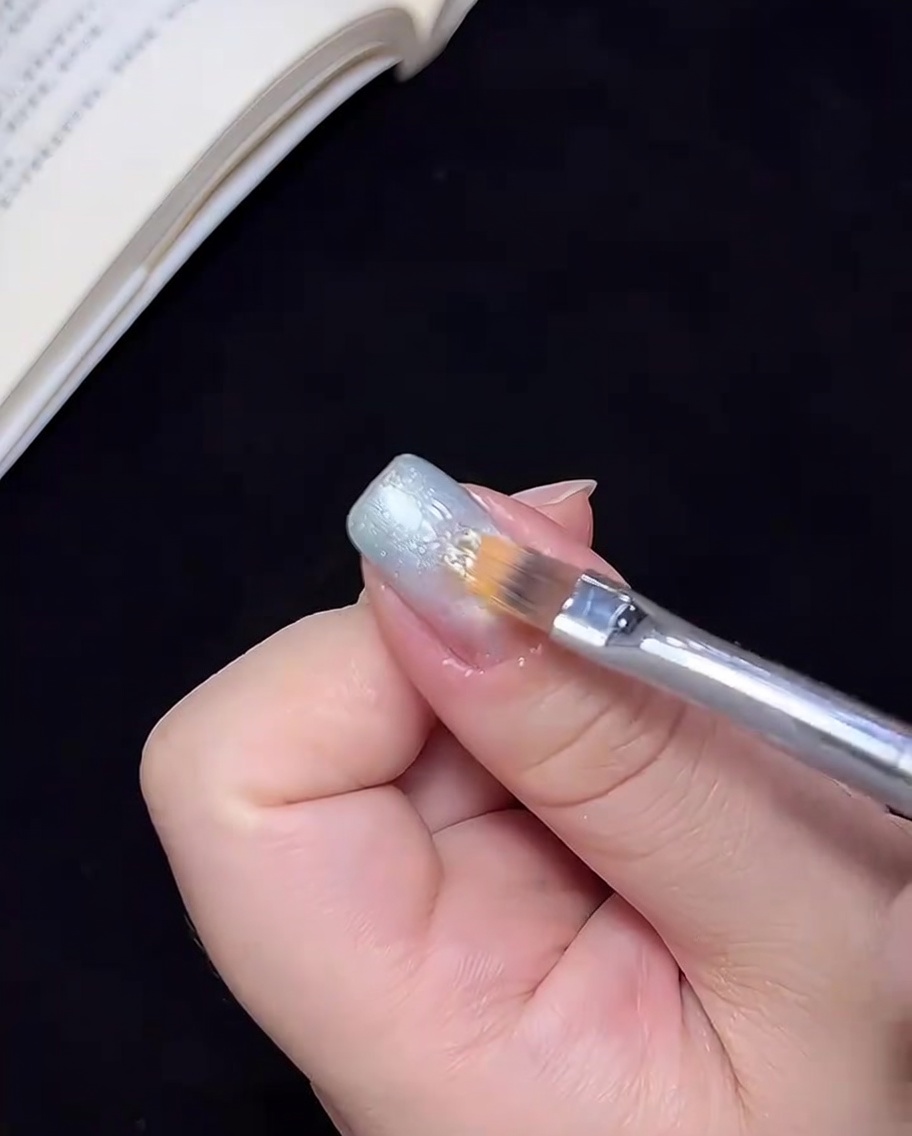Un pincel difuminando el color de gel azul hacia el centro de la uña para crear una transición ombré.