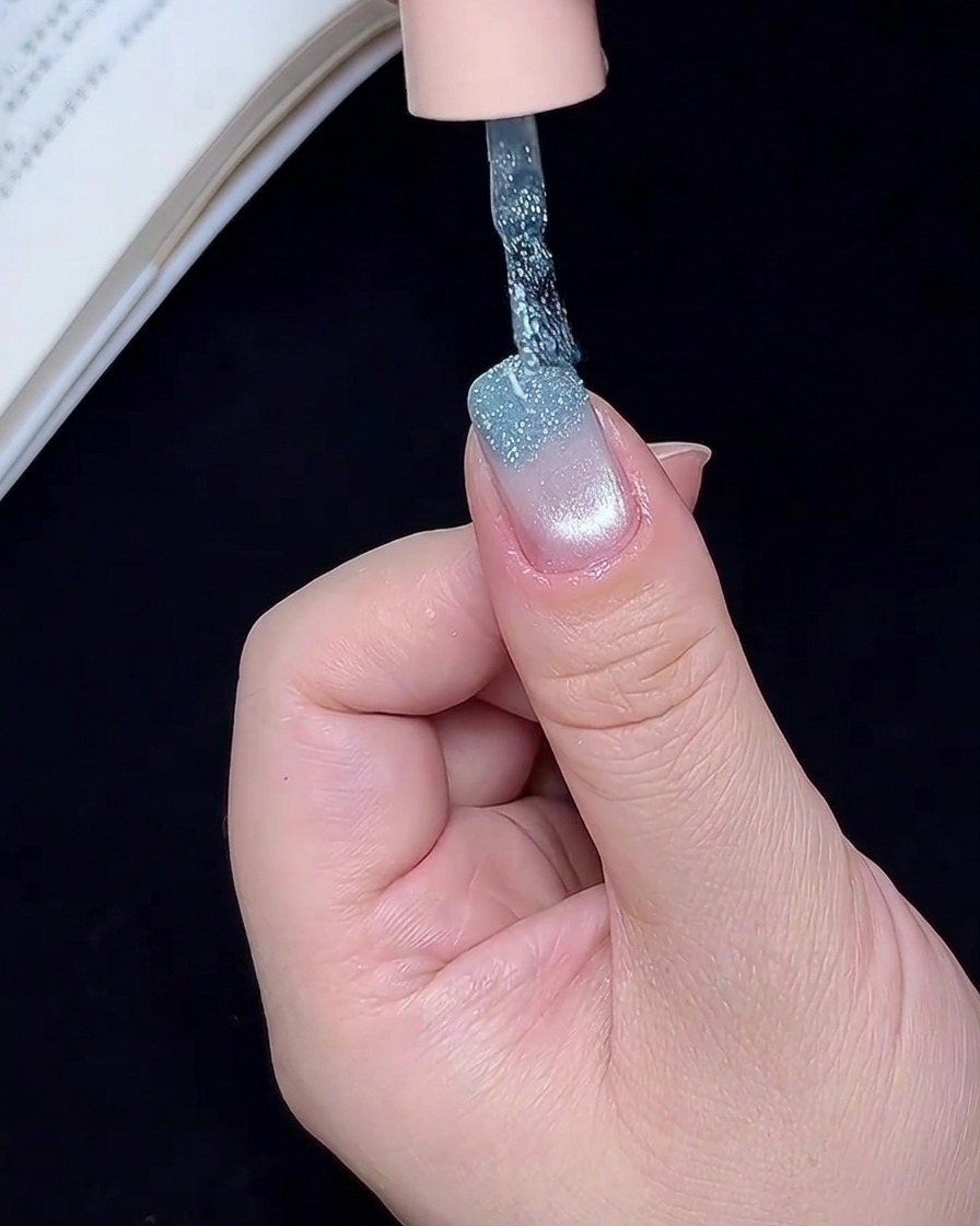 Un pincel de arte de uñas aplicando gel de purpurina azul brillante en el borde libre de una uña.