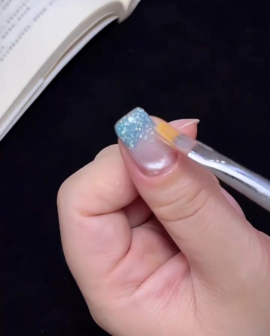 Un pincel limpio arrastrando ligeramente el gel de purpurina azul hacia arriba en la uña para crear un efecto ombré.
