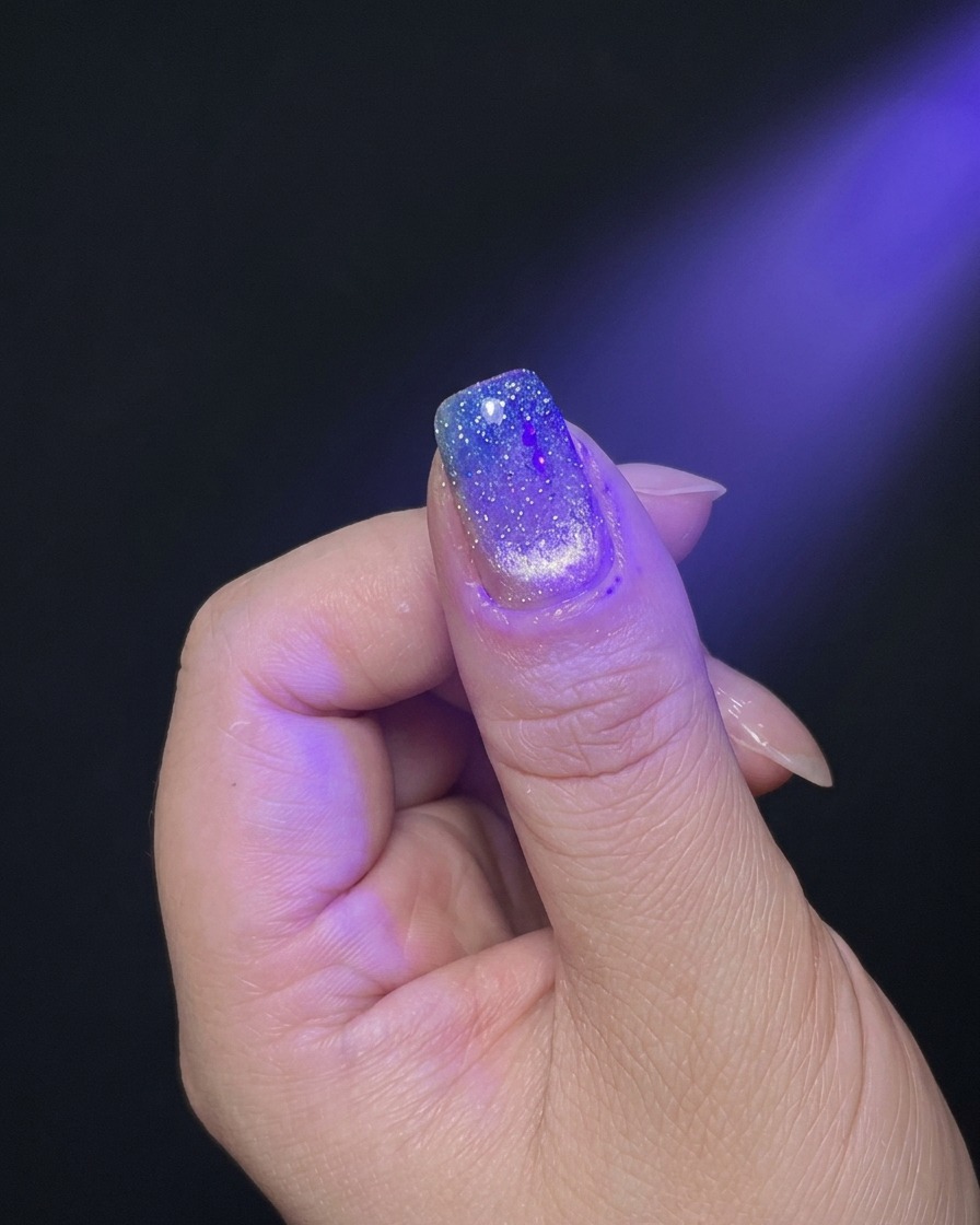 Una mano posicionada bajo la luz púrpura de una lámpara de uñas UV/LED para el curado.
