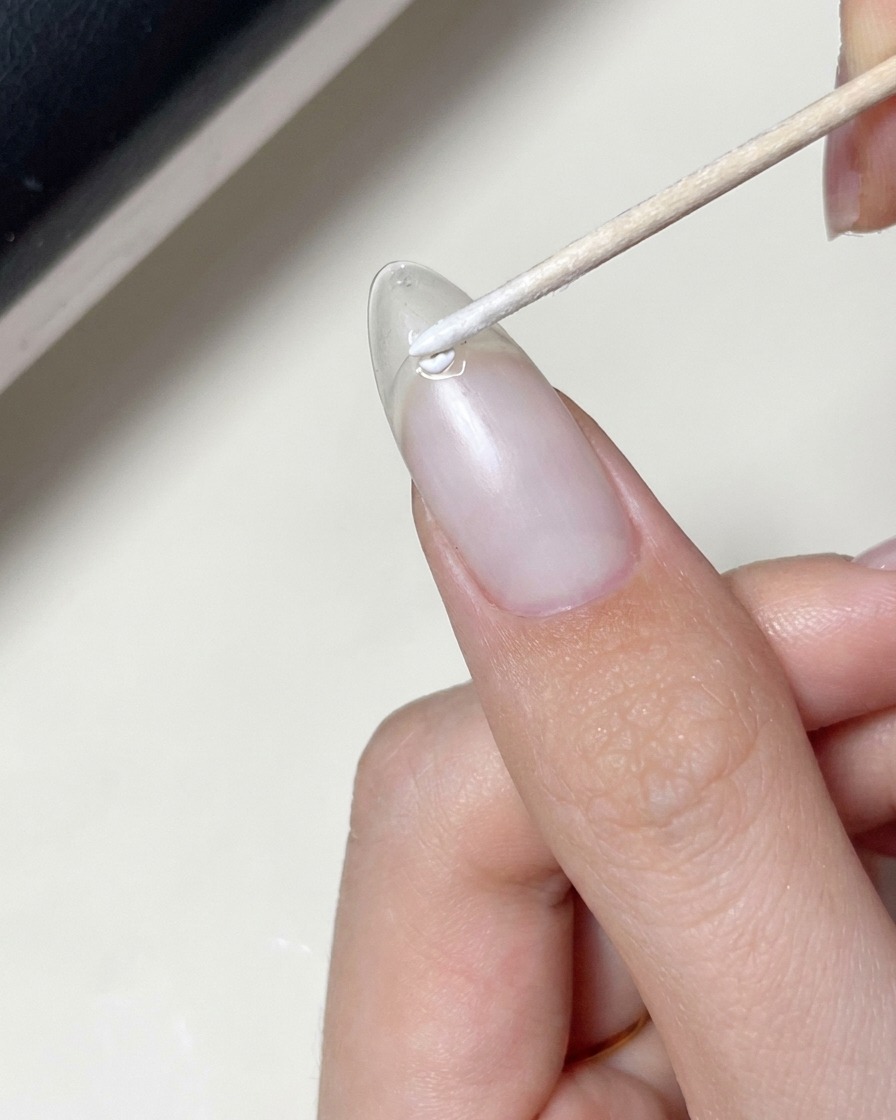 Un pincel aplicando una capa de gel transparente sobre una uña que ya tiene colocada una calcomanía de estrella.