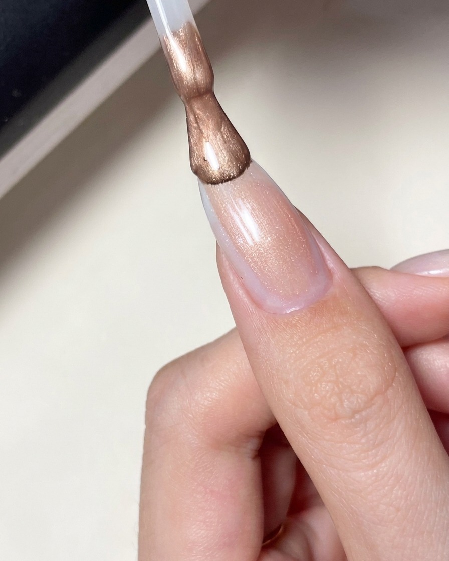 Un pincel aplicando un esmalte de gel rosa lechoso sobre una uña con diseño de estrellas.