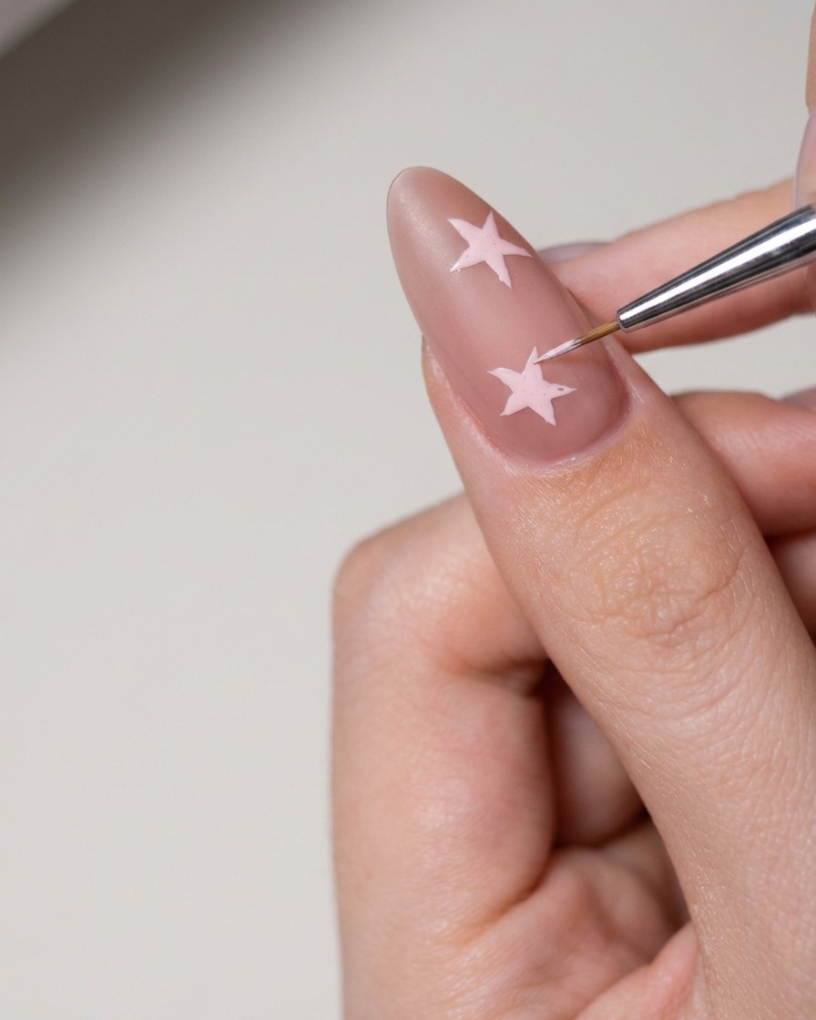 Una pequeña herramienta aplicando pasta de arte de uñas blanca para rellenar una forma de estrella en la uña.