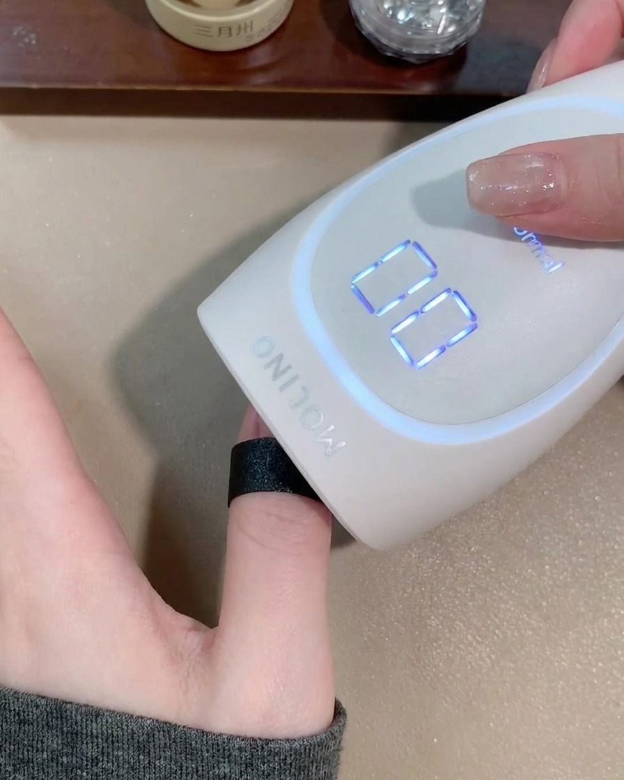 Una mano dentro de una lámpara LED portátil de color blanco mate curando el gel.