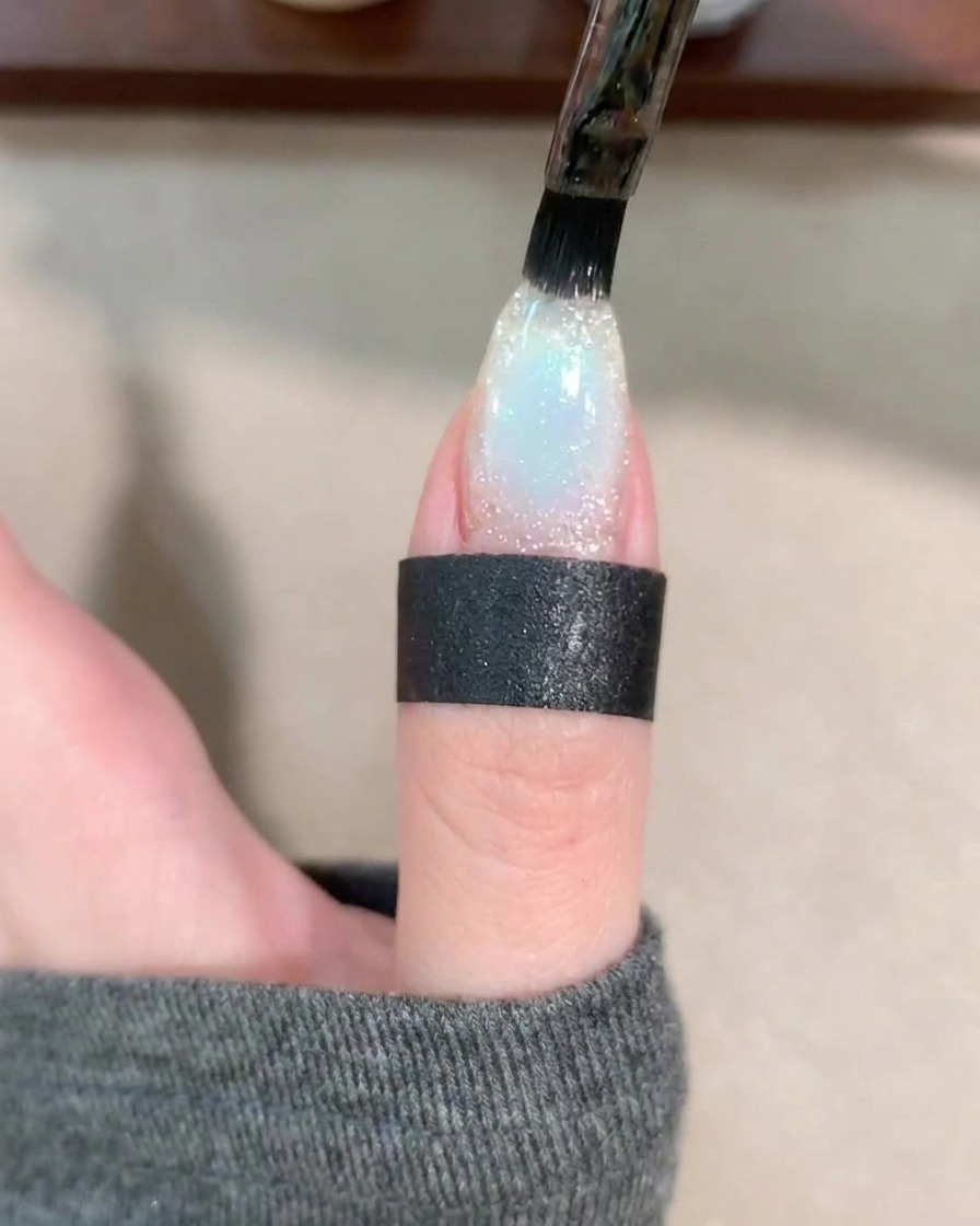 Un pincel de gel aplicando una capa clara de base coat sobre la uña decorada.