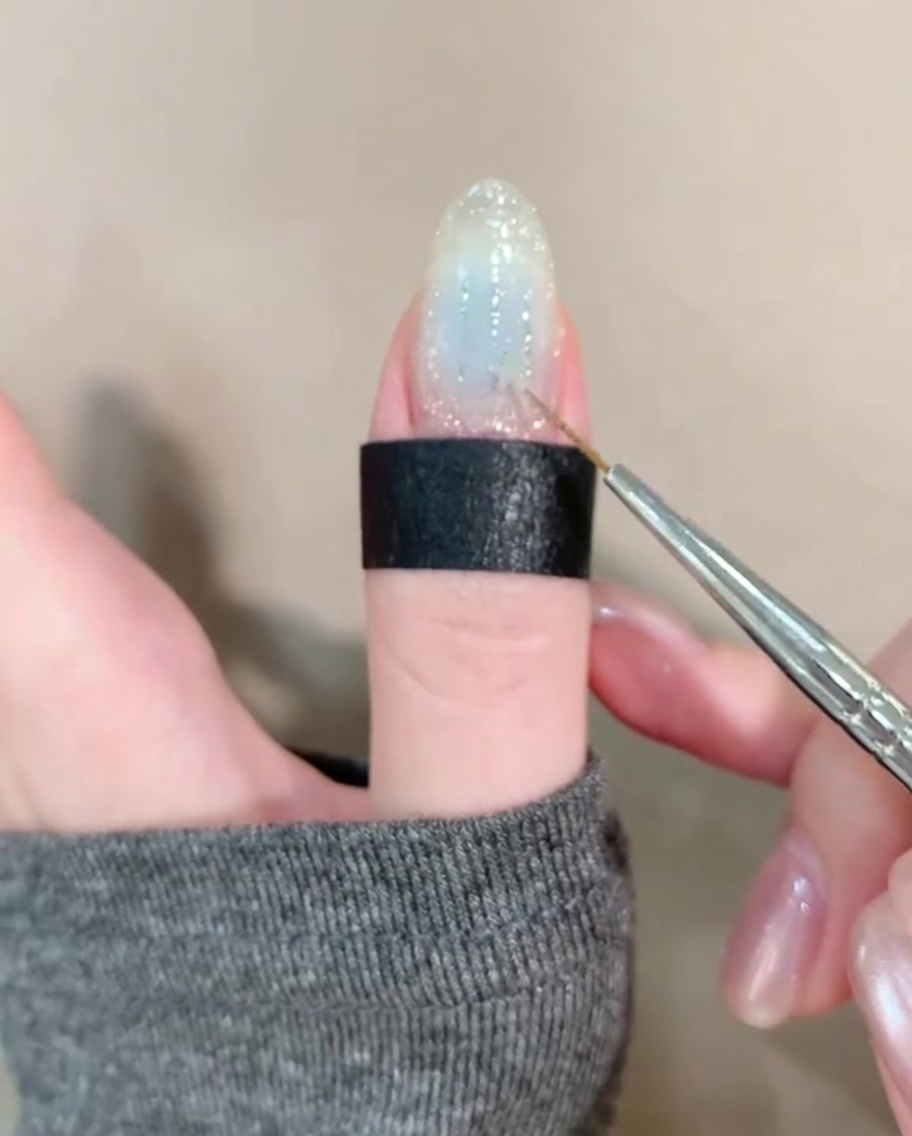 Unas pinzas colocando una pequeña estrella dorada sobre una uña decorada con glitter y tonos azules.
